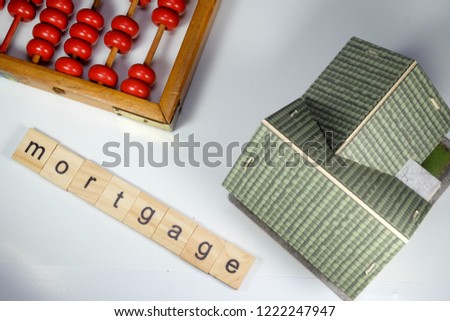 A flatlay picture of house miniature, abacus or chinese calculator and word tile mortgage.