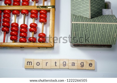 A flatlay picture of house miniature, abacus or chinese calculator and word tile mortgage.