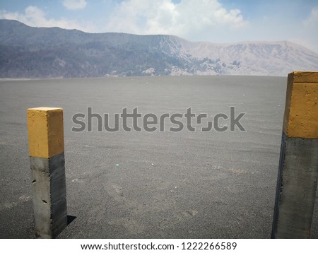 Concrete poles with a yellow stripe stand in the desert with the background of a mountain and cloud blue sky. Located in Bromo Tengger Semeru National Park, East Java, Indonesia.