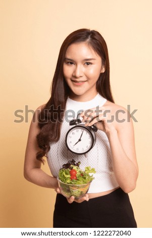 Young Asian woman with clock and salad   on beige background.