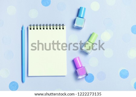 Empty note pad and colorful nail polishes on blue pastel confetti background. Copyspace for text. Bright and festive picture. Top view, flat lay.