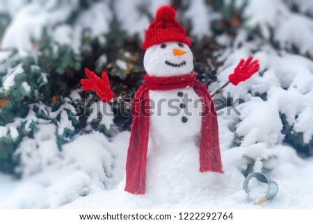 snowman in the forest in Christmas clothes, next to the tree