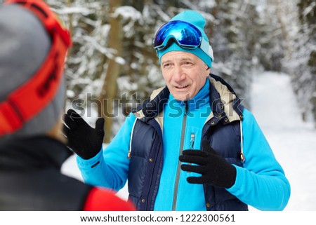 Active senior man in skiing sportswear explaining something to his wife during training in winter forest