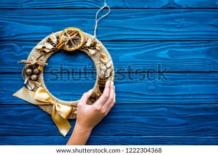 Hand hang a creative christmas wreath made of thread, dry fruits and nuts on blue wooden background top view copy space