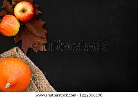 Composition with autumn vegetables and leaves in red and orange colors. Brown dried leaves, pumpkin, apple on black background top view copy space