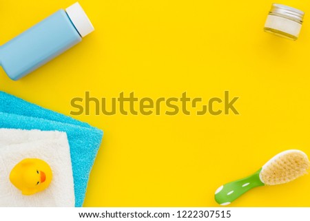Baby care. Bath cosmetics and accessories for child. Shampoo, gel, cream, comb, yellow rubber duck on yellow background top view copy space