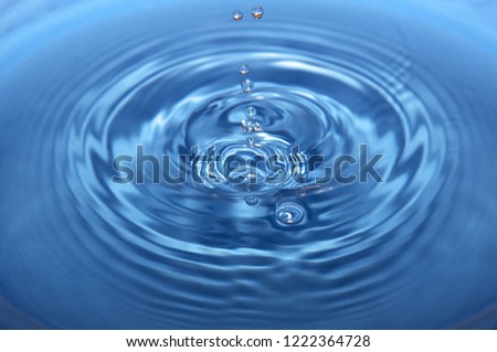 Water drops make a splash with ripples in a blue bowl full of water