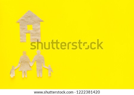 Green energy for home concept. Care for environment. House cutout made of craft paper near family cutout on yellow background top view space for text
