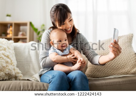 family, technology and motherhood concept - happy young asian mother with little baby son taking selfie by smartphone at home