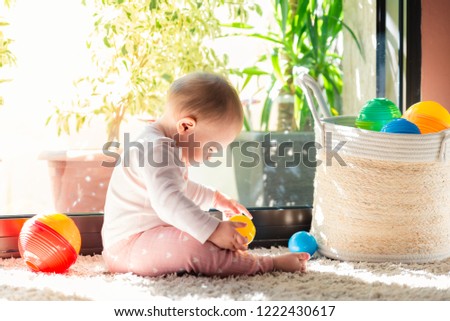 Cute little beautiful baby girl playing with small colorful plastic balls on living room carpet.