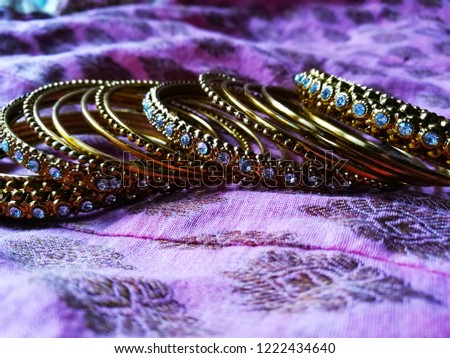 Stock photo of traditional Indian gold designer bangles or bracelet decorated on pink color printed fabric background. Picture captured under natural light at Bangalore karnataka India.