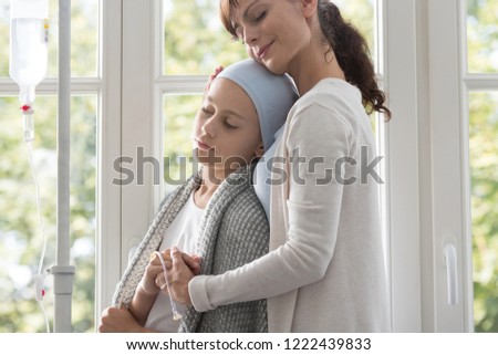 Caregiver hugging sick child with cancer wearing headscarf