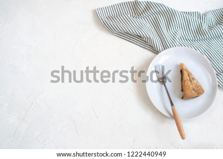 Served plate with portion plum pie on Crumpled Striped Napkin next to cup of matcha tea and fresh plums. Minimal picture. Top view, white background, Flat lay, Copy space.