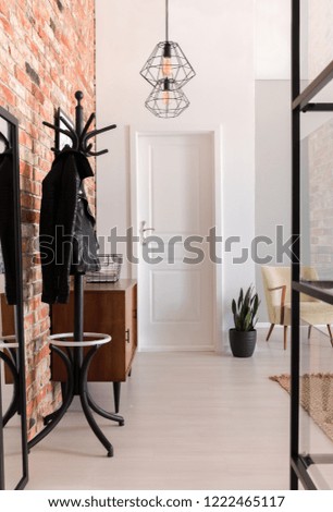 Vertical view of elegant entrance hall with white door and wooden furniture in stylish apartment with brick wall, real photo