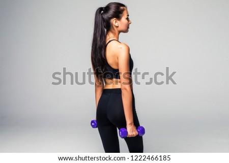 Strong woman working out with dumbbells, flexing her arm. Photo of sporty woman in sportswear on grey background. Rear view