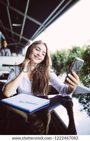 Young woman make notes in notebook while have video call conversation or blogger translation in outdoors cafe