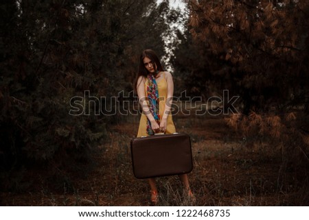 Young beautiful girl in a yellow vintage dress with a vintage suitcase in hand posing in the woods