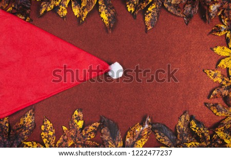 Autumn leaves frame and santa red hat on brown background