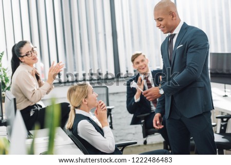 handsome young african american businessman presenting origami flower to happy businesswoman in office 