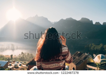 Woman in headphones listening music in nature and looking to mountain with sunrise. One hand setting earphone.
