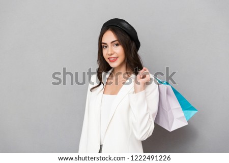 Portrait of a pretty young woman dressed in jacket over gray background, carrying shopping bags