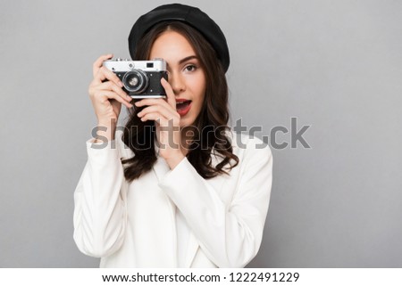 Portrait of a beautiful young woman dressed in jacket over gray background, taking picture with photo camera