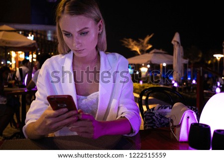 Young woman using smartphone for chatting at night in Dubai Marina. Real lifestyle image.
