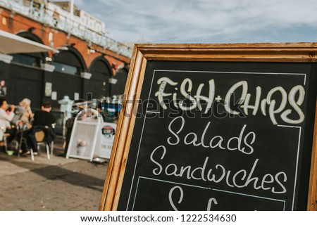 Blackboard with restaurant menus and information in the middle of a promenade, with Fish and Chips, salads, sandwiches and other food. Royalty-Free Stock Photo #1222534630