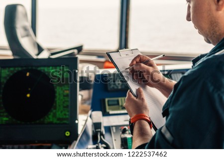 Marine navigational officer or chief mate on navigation watch on ship or vessel. He fills up checklist. Ship routine paperwork Royalty-Free Stock Photo #1222537462