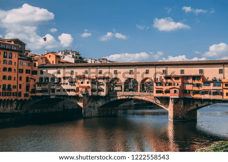 Ponte Vecchio bridge and river Arno in Florence Italy, colorful houses, blue sky with clouds and bird flying, reflection on the water surface