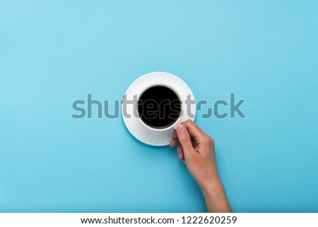 Female hand holding a white cup with black coffee on a pink background. Flat lay, top view