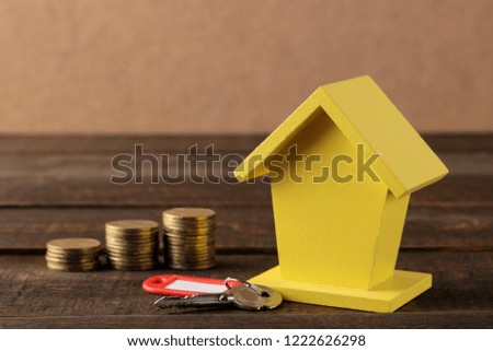 The concept of buying a home. Yellow decorative house and money and keys on a brown background with a place for an inscription.