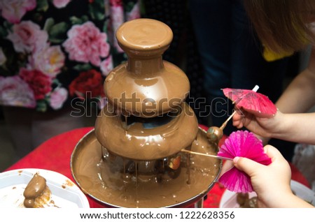 Vibrant Picture of Chocolate  Fontain on children kids birthday party with a kids playing around and marshmallows and fruits dip dipping into fountain.Chocolate fountain placed on a table in w