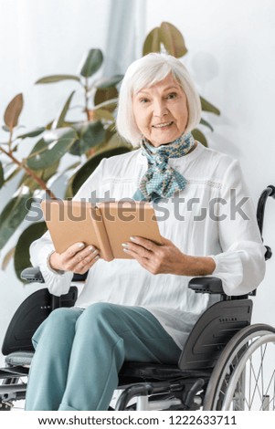 happy senior woman sitting in wheelchair and reading book