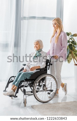 young woman pushing wheelchair with senior woman in nursing home