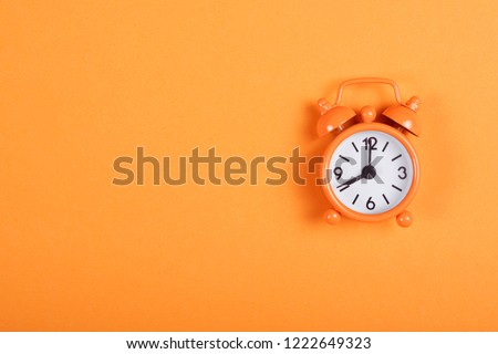 Orange analogue alarm clock showing eight in the morning on background of the same tone. Flat lay with copy space.
