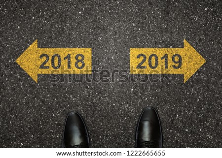 Businessman is looking down at his feet on a Asphalt road with choice arrows and 2018 and 2019 number painted on the surface. Concept for success in the future goal and passing time. Happy new year Royalty-Free Stock Photo #1222665655