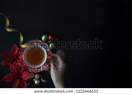 Moody Dark Christmas morning. Christmas Tea Flatlay on BlackTable. Christmas Flatlay with Copy Space. Hand holding Tea Cup. Dark food photography Christmas.
