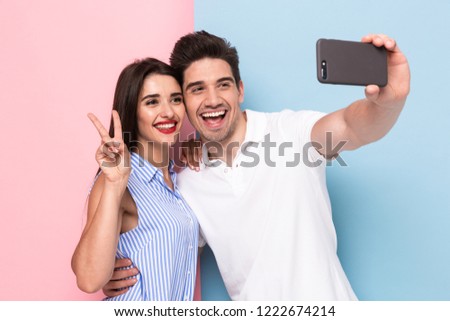 Image of positive man and woman taking selfie photo on mobile phone isolated over colorful background