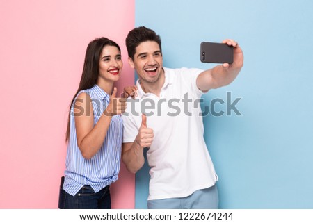 Image of caucasian couple using mobile phone and taking selfie photo isolated over colorful background
