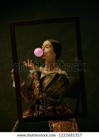 Portrait of a girl wearing a princess or countess dress over dark studio. portrait through picture frame with bubble gum