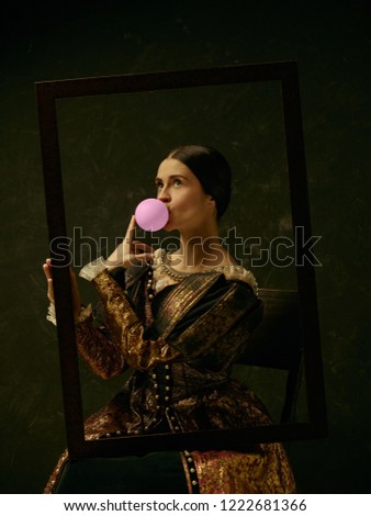 Portrait of a girl wearing a princess or countess dress over dark studio. portrait through picture frame with bubble gum