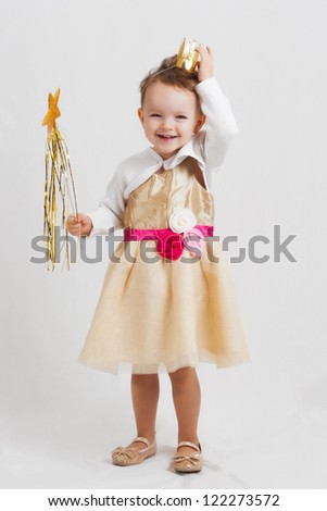 portrait of an happy smiling and laughing little blonde girl with a crown wearing a princess costume and holding a wand