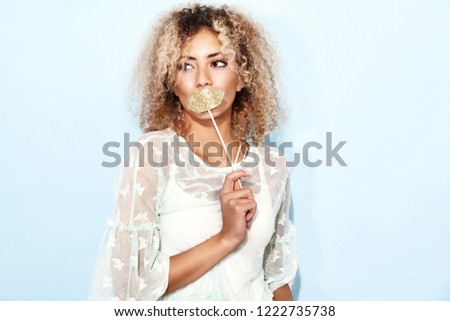 Portrait of blissful lovable woman with blond african hairstyle with big lips on stick. Smiling model girl in trendy summer clothes posing on blue background 