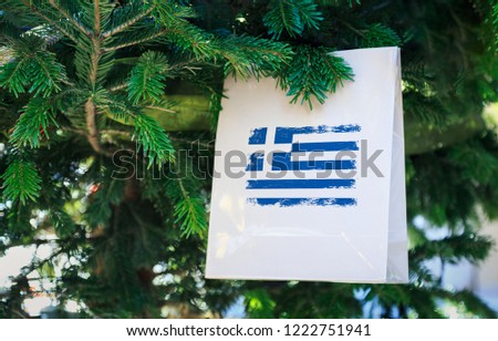 Greece flag printed on a Christmas shopping bag. Close up of a shopping bag as a decoration on a Xmas tree on a street. New Year or Christmas shopping, local market sale and deals concept. 