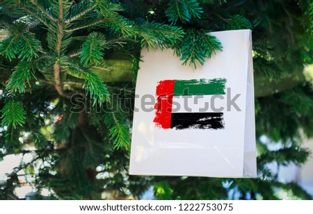 UAE flag printed on a Christmas shopping bag. Close up of a shopping bag as a decoration on a Xmas tree on a street. New Year or Christmas shopping, local market sale and deals concept. 