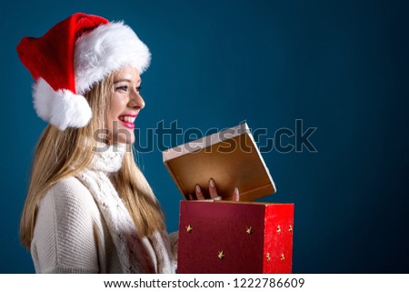 Young woman with santa hat opening a Christmas gift box on a dark blue background