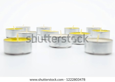 A set of white and yellow tealight paraffin candle lies on a white background with a clipping path.