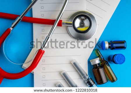 Medical syringe, stethoscope, vials, ampule and notebook on blue background with selective focus and crop fragment