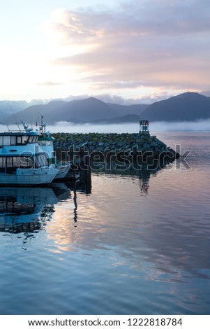Sea smoke on sunrise of Sitka Alaska harbor, piers with docked boats. clouds and pink sky reflecting on pacific ocean
